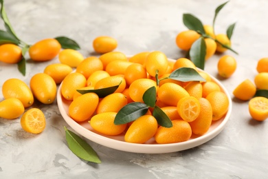 Photo of Fresh ripe kumquats in plate on light grey table