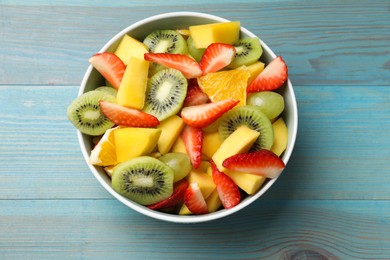 Tasty fruit salad in bowl on light blue wooden table, top view