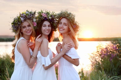 Photo of Young women wearing wreaths made of beautiful flowers outdoors at sunset