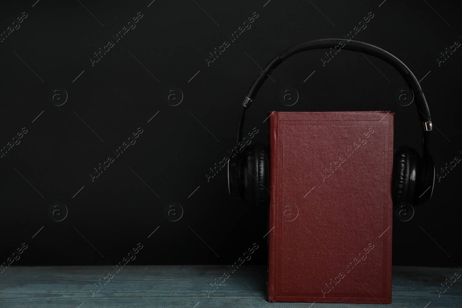 Photo of Book and modern headphones on wooden table against black background. Space for text