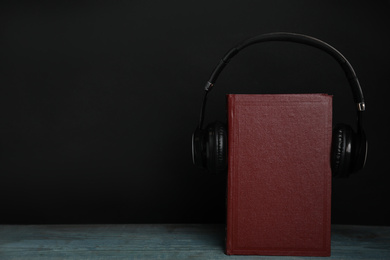 Photo of Book and modern headphones on wooden table against black background. Space for text