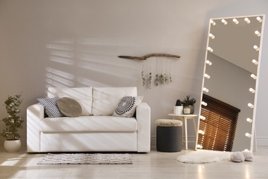 Stylish mirror with light bulbs and comfortable sofa in living room. Interior design