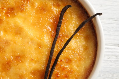 Photo of Delicious creme brulee and vanilla sticks on white wooden table, top view