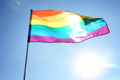 Photo of Rainbow LGBT flag fluttering on blue sky background. Gay rights movement