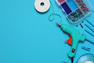 Photo of Hot glue gun and handicraft materials on light blue background, flat lay. Space for text