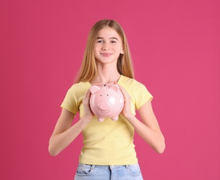 Teen girl with piggy bank on color background