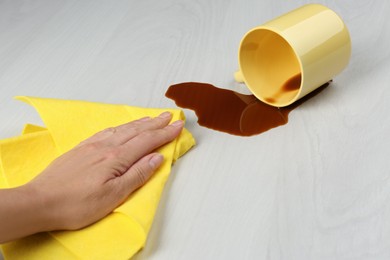 Photo of Woman cleaning spilled coffee on white wooden table, closeup