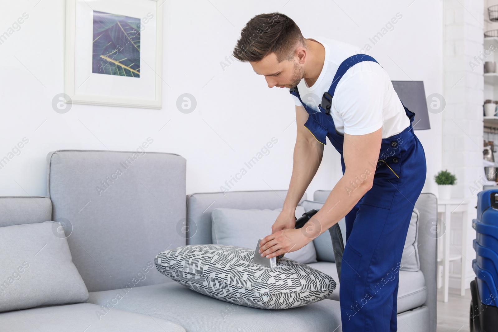 Photo of Male worker removing dirt from sofa with professional vacuum cleaner indoors