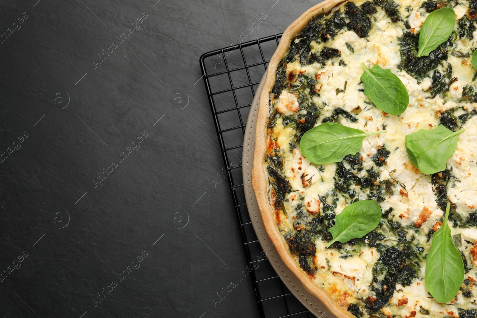Photo of Delicious homemade spinach quiche on black table, top view. Space for text