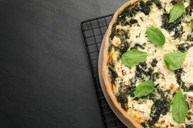 Delicious homemade spinach quiche on black table, top view. Space for text