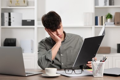 Photo of Tired young man working at table in office. Deadline concept