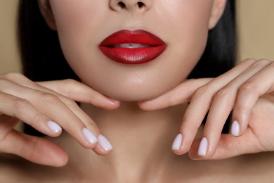 Photo of Young woman wearing beautiful red lipstick on beige background, closeup