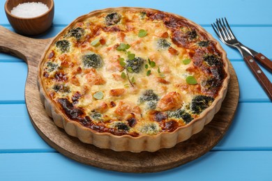 Delicious homemade quiche with salmon and broccoli on light blue wooden table