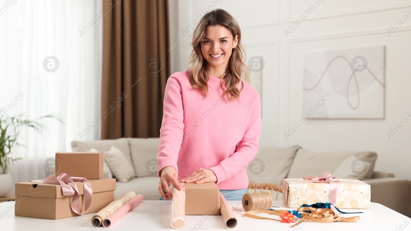 Photo of Beautiful young woman wrapping gift at table in living room