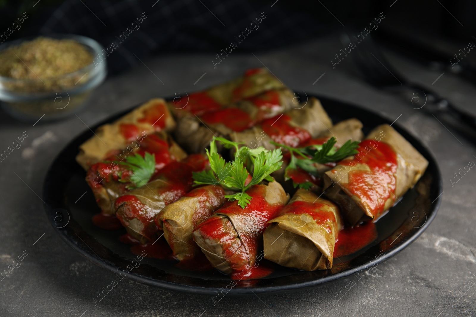 Photo of Delicious stuffed grape leaves with tomato sauce on grey table