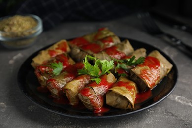 Delicious stuffed grape leaves with tomato sauce on grey table