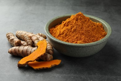 Bowl with turmeric powder and raw roots on grey table