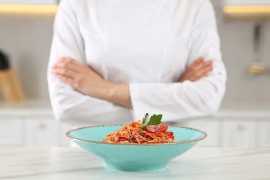 Photo of Closeup of chef with crossed arms near delicious spaghetti in kitchen, focus on food