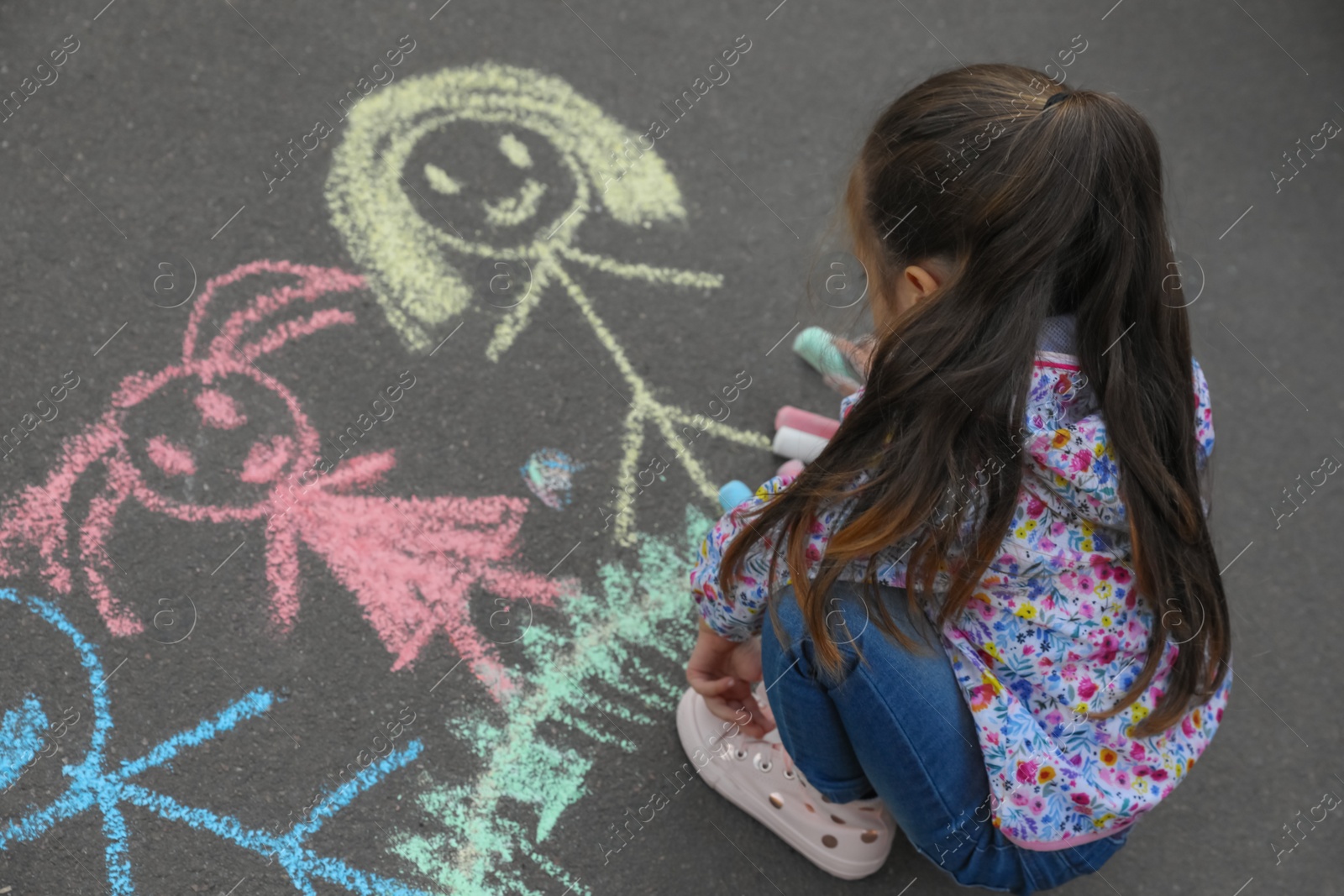 Photo of Child drawing family with chalk on asphalt
