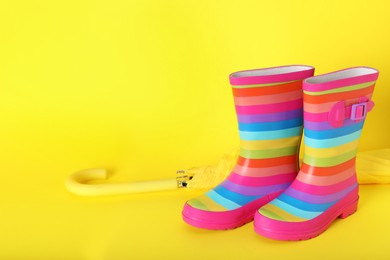 Photo of Pair of striped rubber boots near umbrella on yellow  background. Space for text