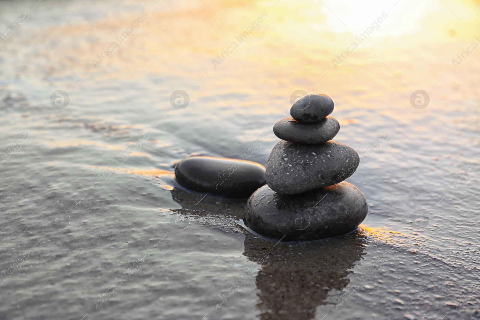 Photo of Dark stones on sand near sea at sunset, space for text. Zen concept