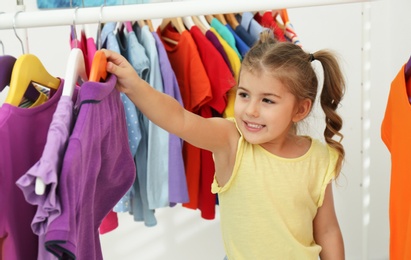 Little girl choosing clothes on rack indoors