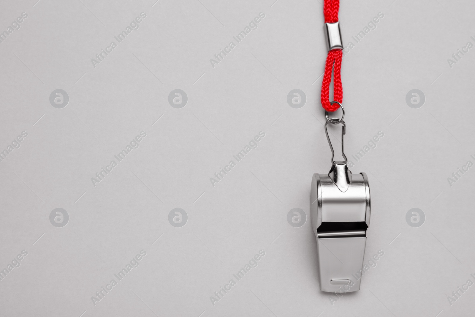 Photo of One metal whistle with red cord on light grey background, top view. Space for text