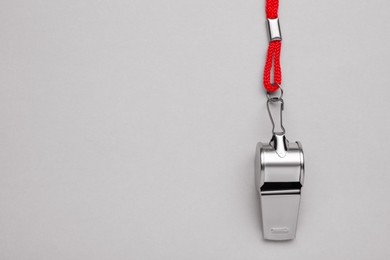 One metal whistle with red cord on light grey background, top view. Space for text