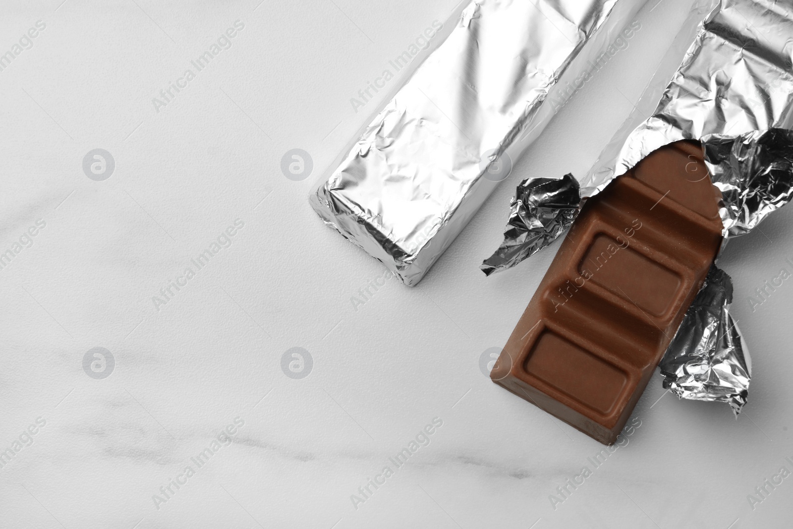 Photo of Tasty chocolate bars wrapped in foil on white table, flat lay. Space for text