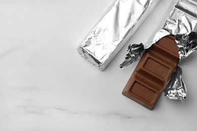 Tasty chocolate bars wrapped in foil on white table, flat lay. Space for text