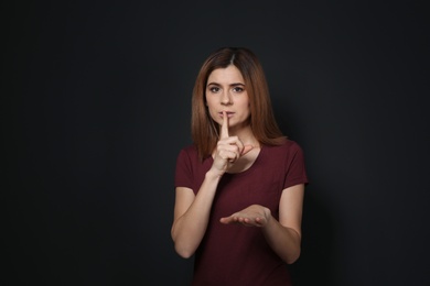 Photo of Woman showing HUSH gesture in sign language on black background