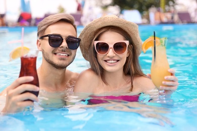 Young couple with cocktails in pool on sunny day