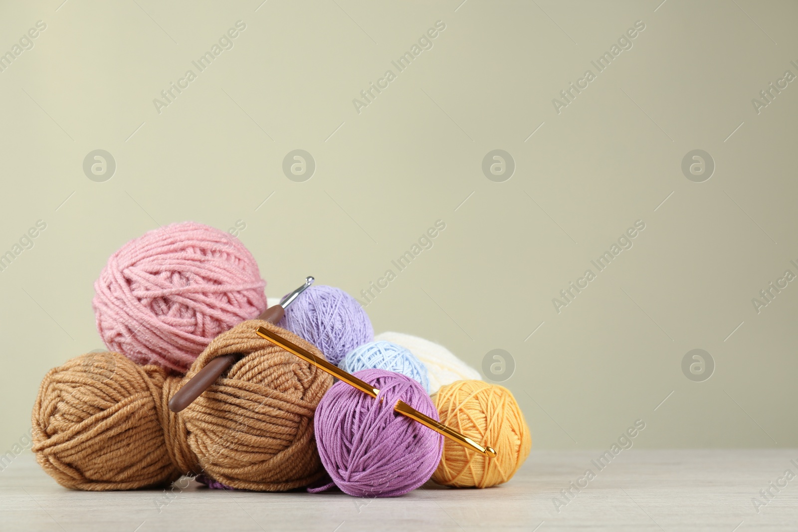 Photo of Clews of colorful knitting threads and crochet hooks on white wooden table against beige background. Space for text