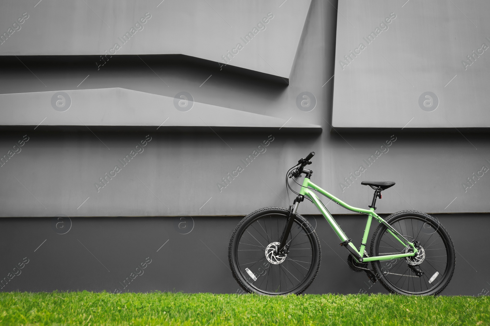 Photo of New modern color bicycle near dark grey wall outdoors