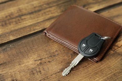 Car key and leather wallet on wooden background. Space for text