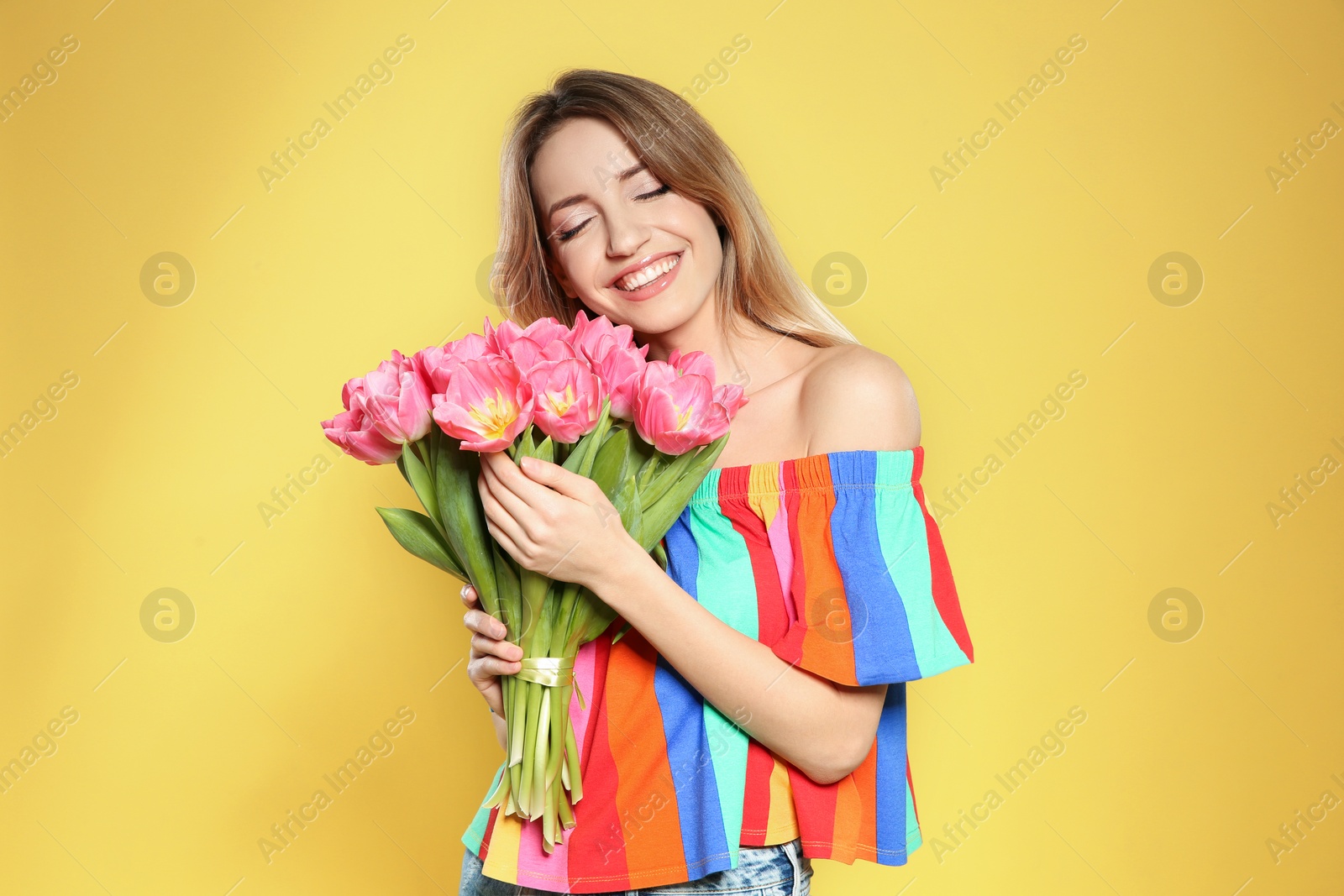 Photo of Portrait of beautiful smiling girl with spring tulips on yellow background. International Women's Day