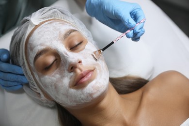 Photo of Cosmetologist applying mask on client's face in spa salon, top view