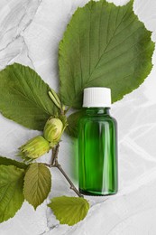 Bottle of essential oil and hazelnut tree twig on white table, flat lay