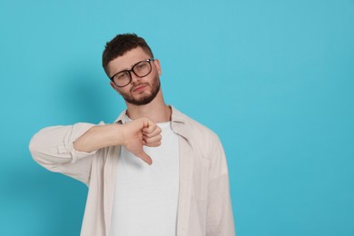 Photo of Young man showing thumb down on light blue background, space for text
