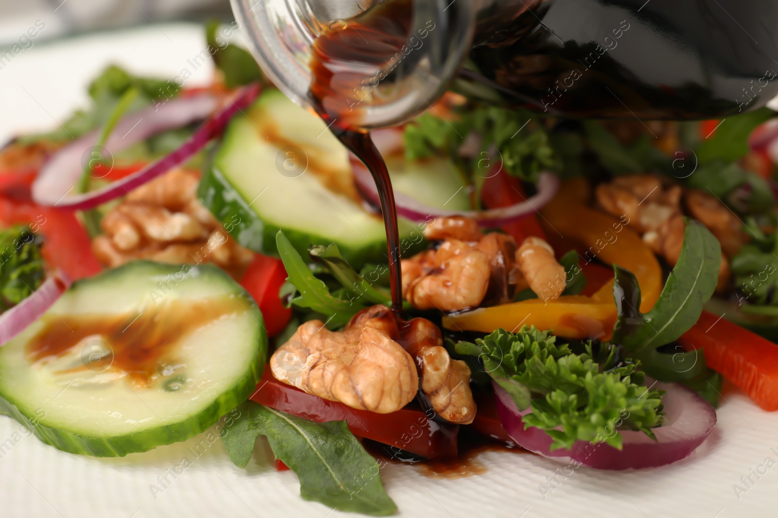 Photo of Pouring balsamic vinegar onto vegetable salad, closeup