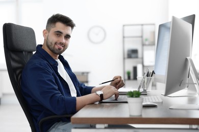 Photo of Happy young programmer working with laptop in office