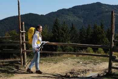Woman with trekking poles near wooden fence enjoying mountain landscape