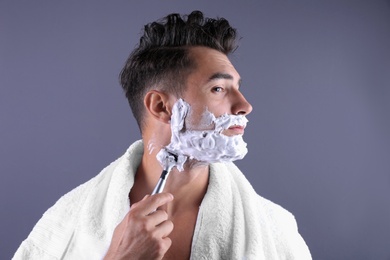 Handsome young man shaving on color background