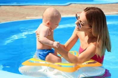 Happy mother with little baby in swimming pool on sunny day