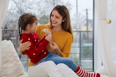 Happy mother and daughter with paper snowflake near window indoors