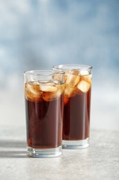 Photo of Glasses of cold cola on table against color background. Space for text