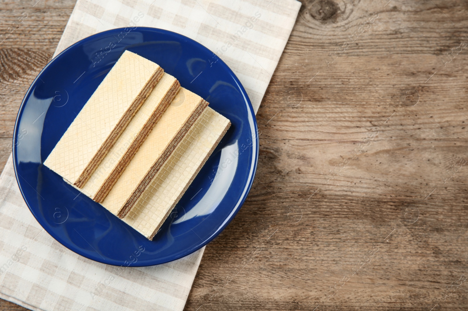 Photo of Plate of delicious wafers on brown wooden background, top view. Space for text