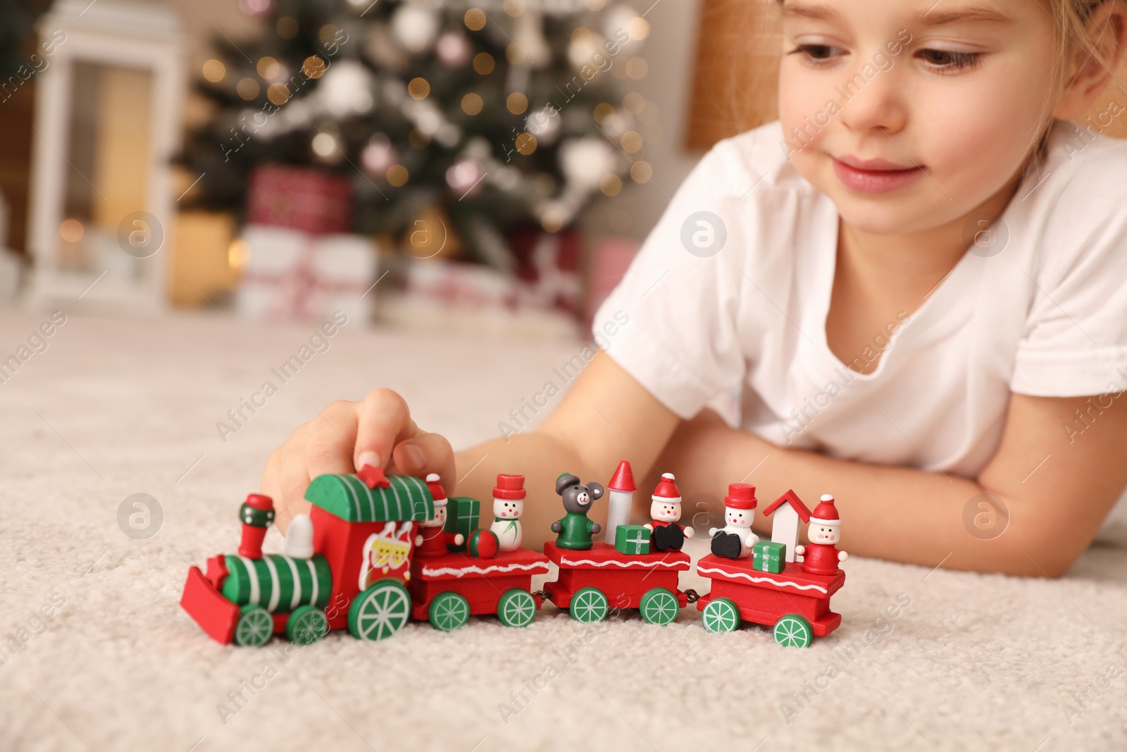 Photo of Little girl playing with colorful train toy in room decorated for Christmas