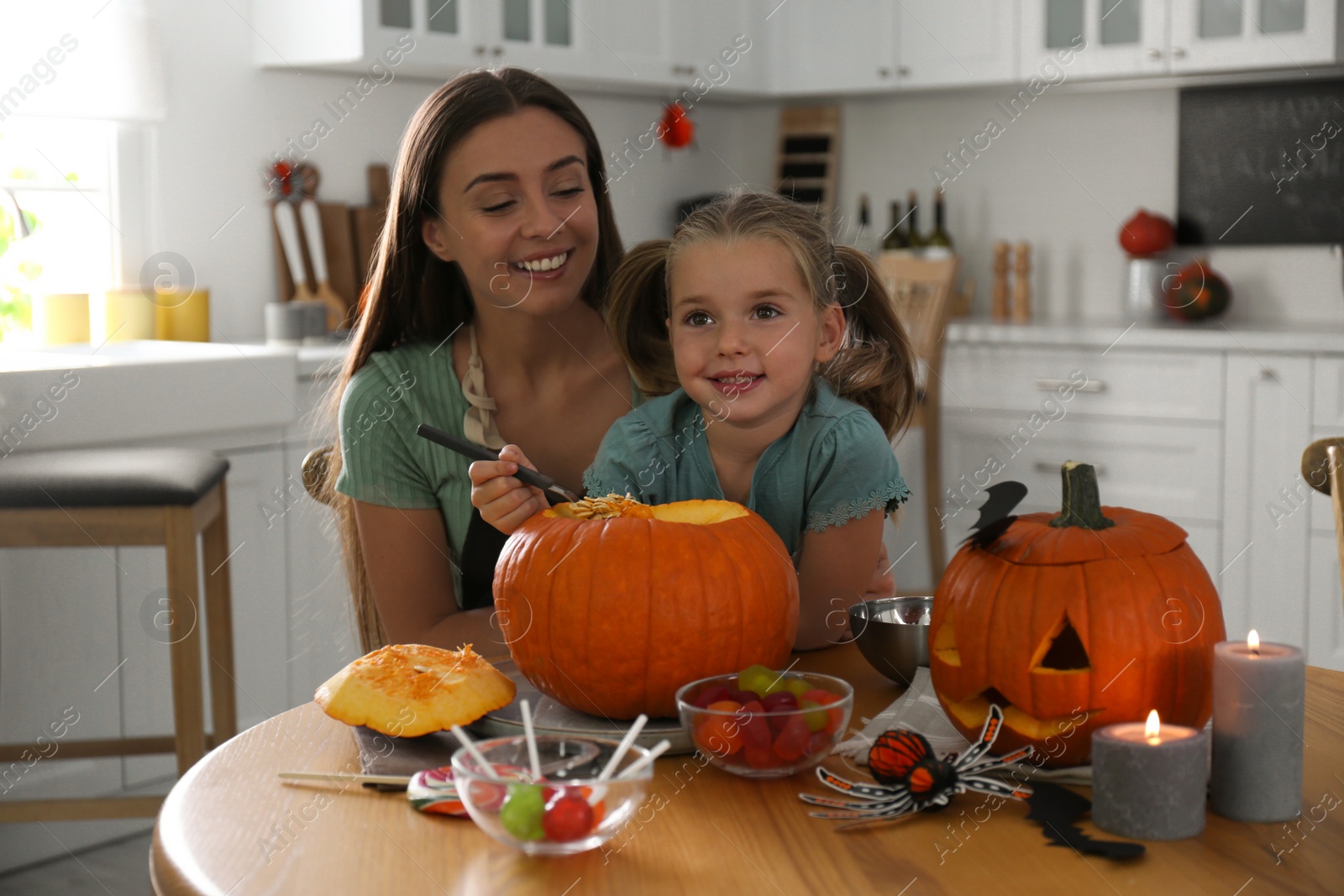 Photo of Mother and daughter making pumpkin jack o'lantern at table in kitchen. Halloween celebration