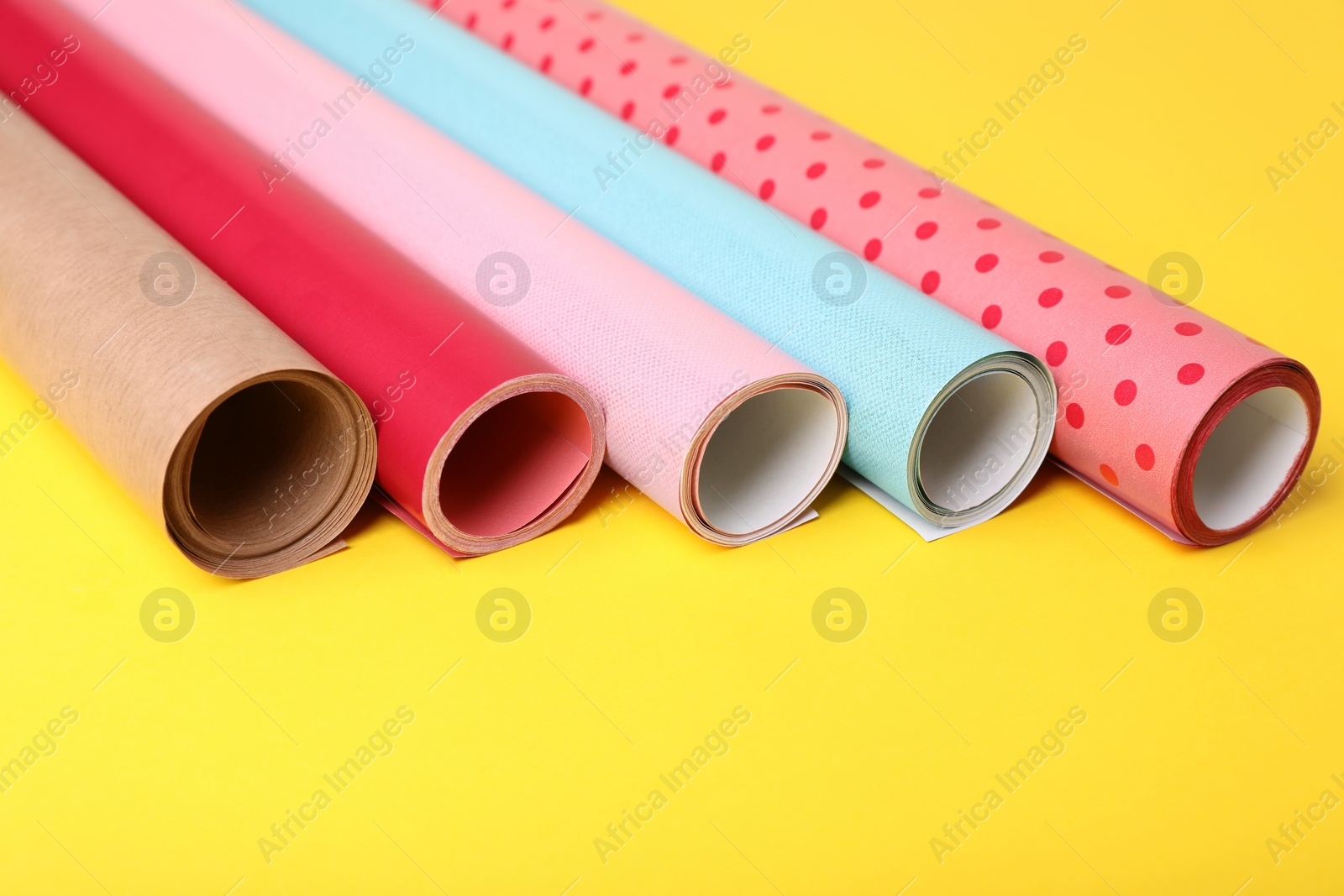 Photo of Rolls of colorful wrapping papers on yellow background, closeup